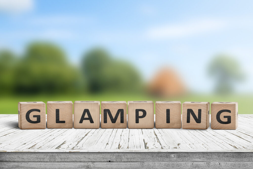 Glamping sign on wooden planks in the summer with a green camping area in the background