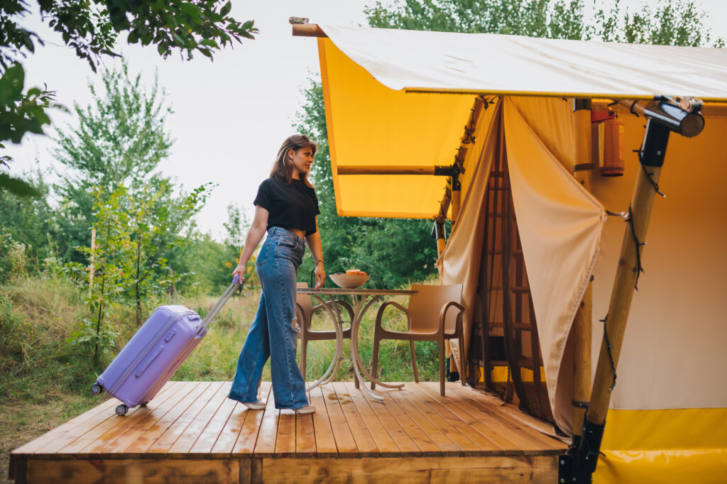 Woman traveler with luggage moving towards bedroom of cozy glamping house. Luxury camping tent for outdoor summer holiday and vacation. Lifestyle concept