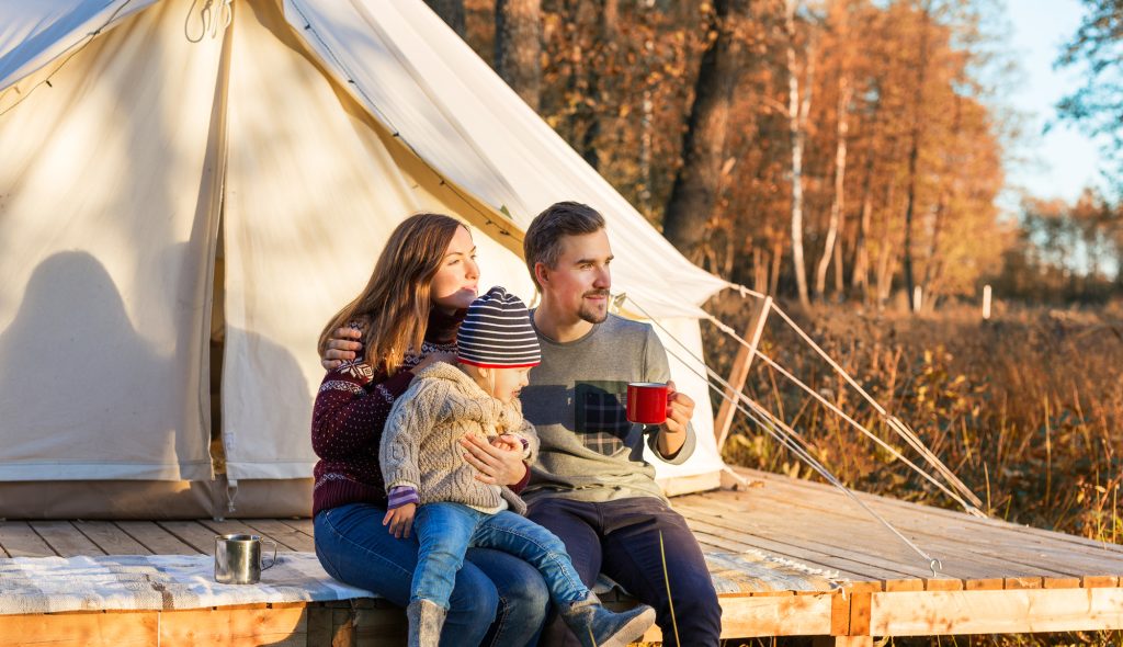 Happy family drinking coffee while sitting near canvas bell tent in the morning in a forest